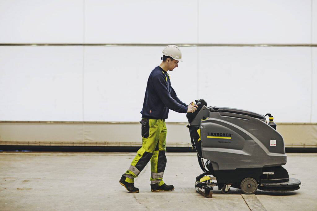 Man i arbetskläder drar städmaskin genom lokal