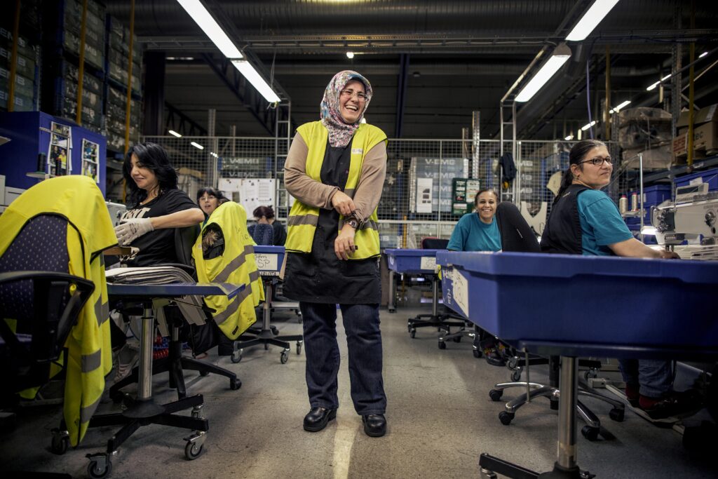 Kvinnor sitter och syr. I mitten står en kvinna och skrattar