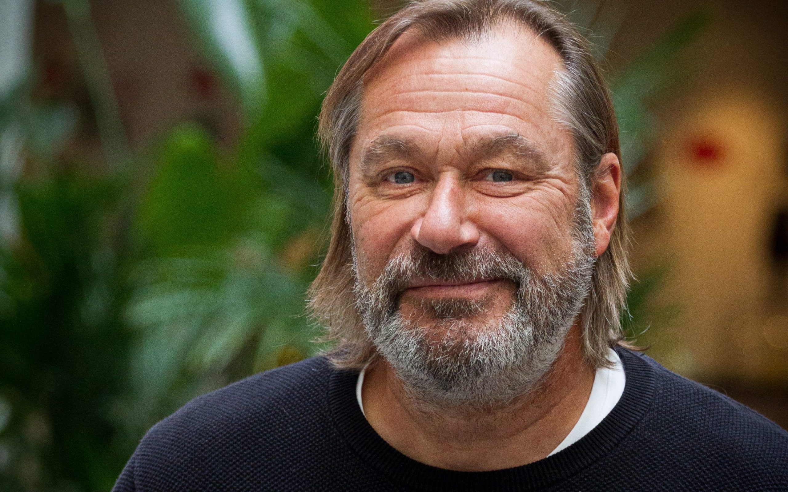 En man med halvlångt hår och skägg framför en växt