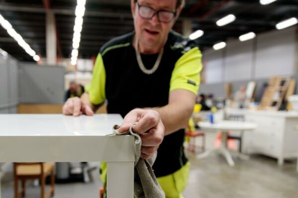 En person i arbetskläder putsar ett bord i närbild