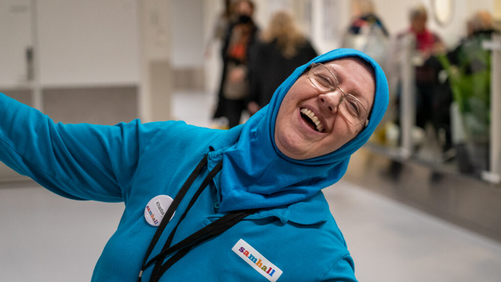 Kvinna i blå kläder och sjal lutar sig bakåt och skrattar