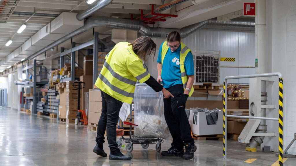 Personer med arbetskläder i lagerlokal. En pekar på golvet