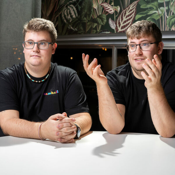 Bild på tvillingarna Linus och Pontus som sitter lutade över ett bord. De har båda två glasögon och bär svarta tröjor. 