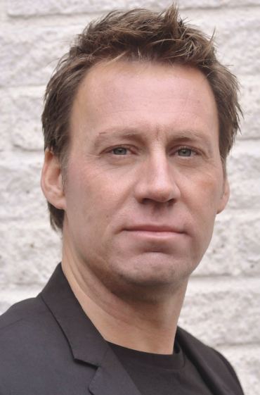 Porträtt av Dan-Olof Rooth. Tittar in i kameran och bär svart kostym. Har brunt hår. 