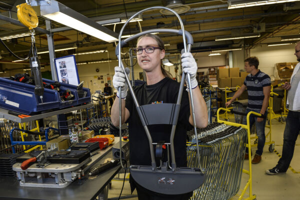 Person med långt hår i hästsvans och glasögon jobbar i ett rum