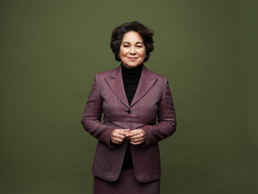 Porträtt av en kvinna med kort mörkt lockigt hår och mörkröd kostym