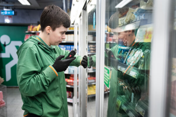 Nora Mångsén scannar varor i en kyl i butiken med ett verktyg. Hon bär gröna arbetskläder.