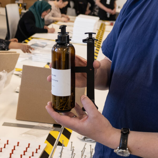 Bild på en hand som håller i tvålpumpen. den har mörkbrun plast och en svart hållare.