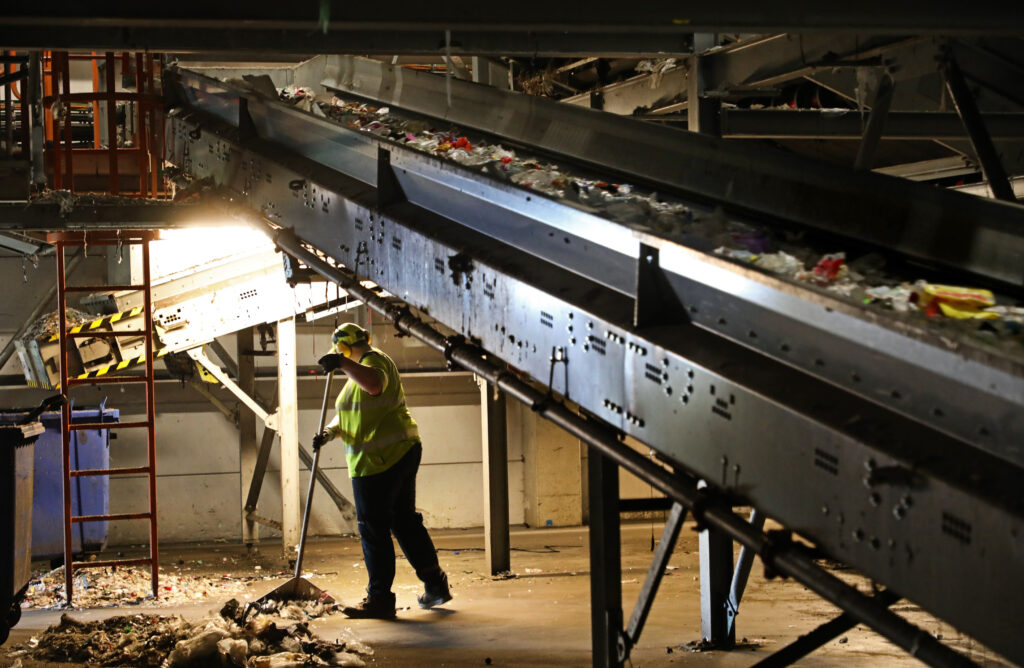 Bild på arbetare som sopar skräp på instustrigolvet. det är mörkt i lokalen. 