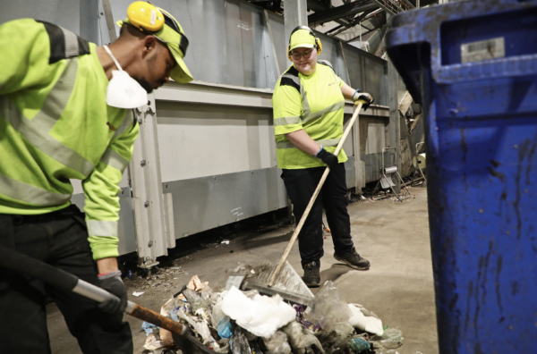 Samhall-medarbetaren Kubrom Masho och Jennifer Sjöberg bär reflexkläder och sopar skräp på marken med skyfflar. 