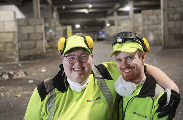 Jennifer Sjöberg och Eric Hjertz står bredvid varandra. De bär arbetskläder i reflexgult. De ler och ser in i kameran.