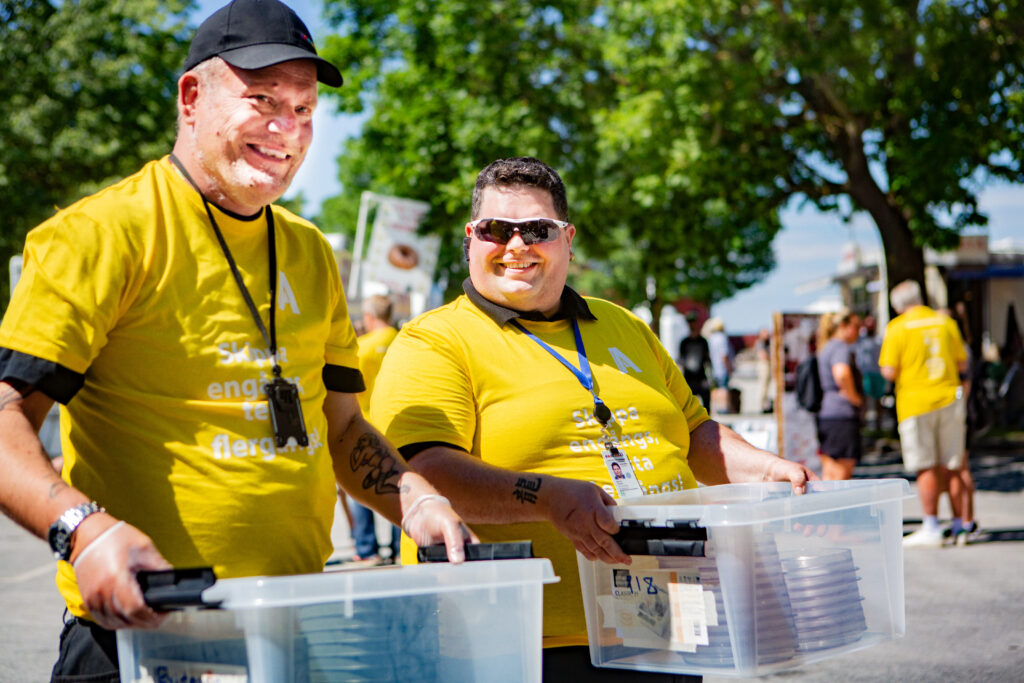 En bild på två Samhall-medarbetare som bär på varsin plastlåda.