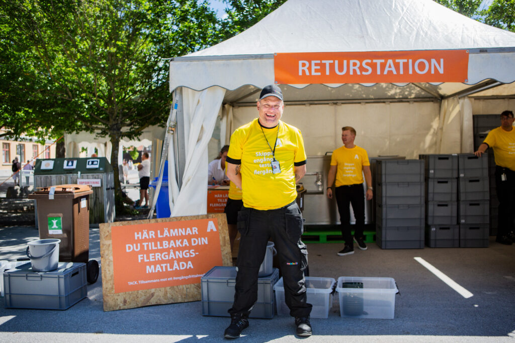 En person står utanför ett partytält i Almedlen och tittar in i kameran och ler. Han bär svart keps och gul T-shirt. 