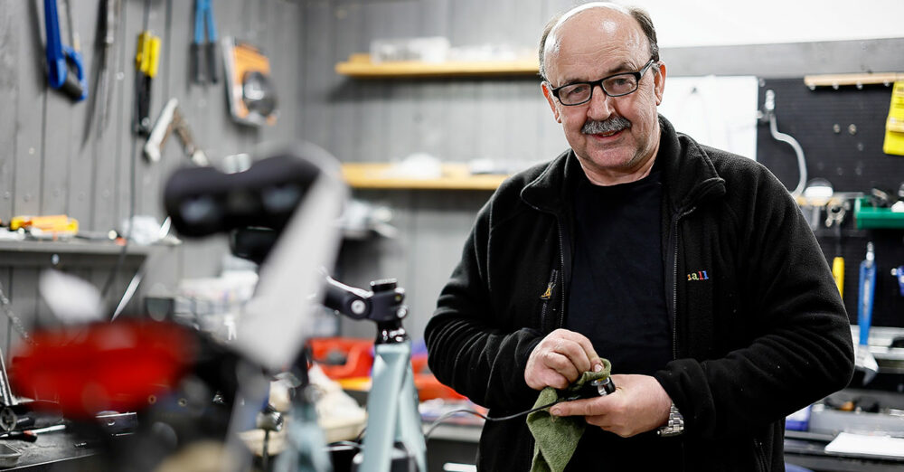 Man med glasögon och stor mustasch står i en verkstad och putsar ett verktyg