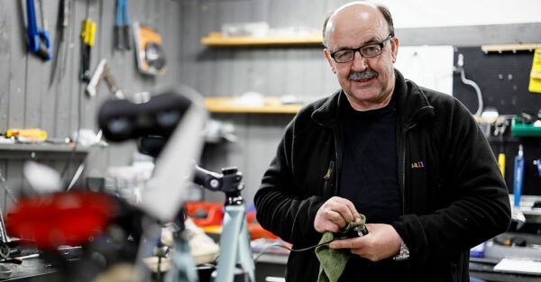 Man med glasögon och stor mustasch står i en verkstad och putsar ett verktyg