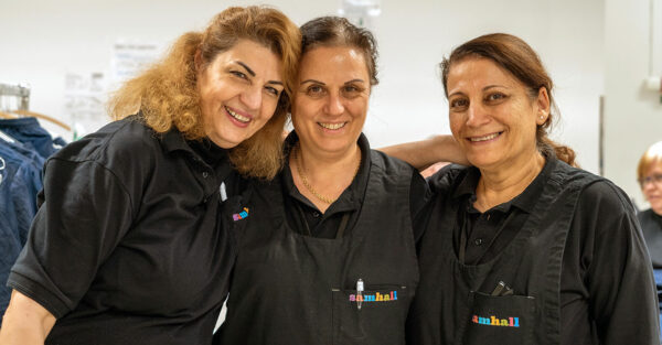 Tre personer ler och tittar in i kameran. De bär svarta arbetskläder.