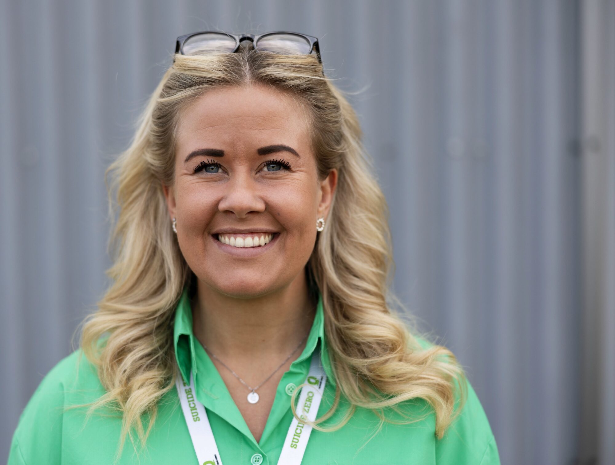 Porträtt på Charlotte. Hon ler och tittar in i kameran. Hon har blont hår och glasögon på huvudet.