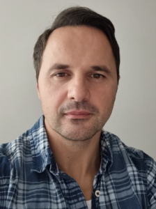 Porträtt av Valon Hetemi som tittar in i kameran. Han bär en rutig skjorta. 