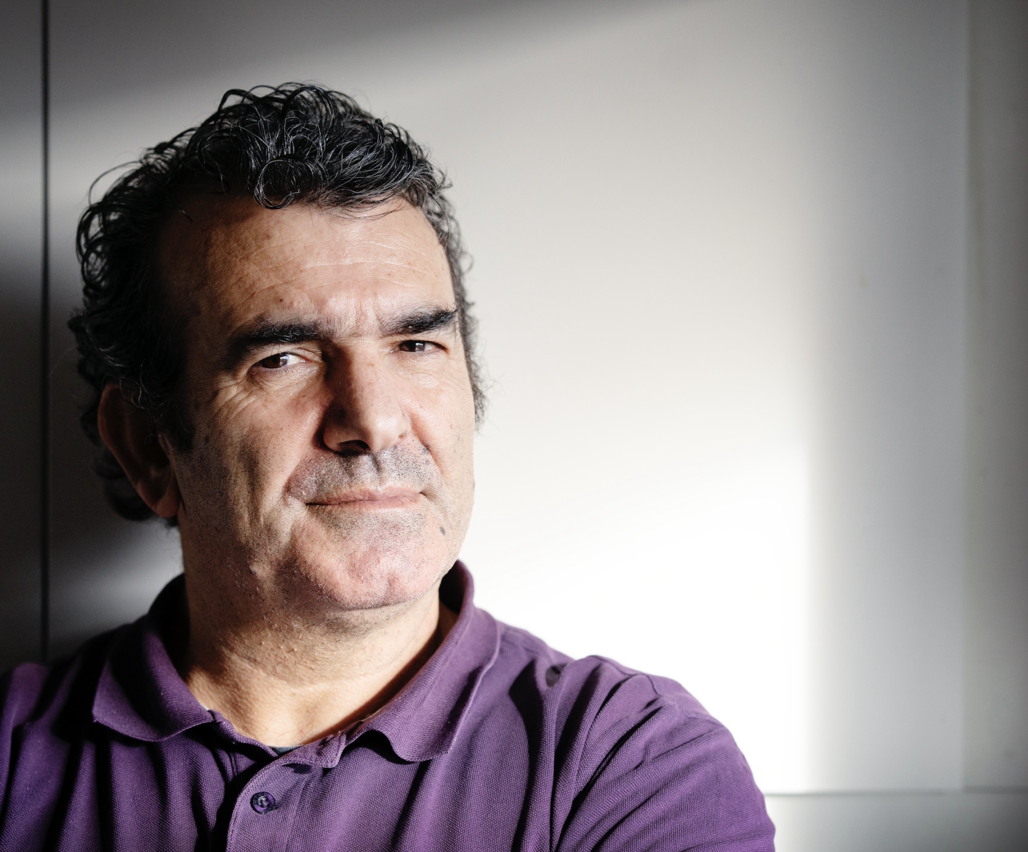 Porträttbild på Parvis Alizadeh. Han står framför en vit bakgrund och hans pikétröja är lila.