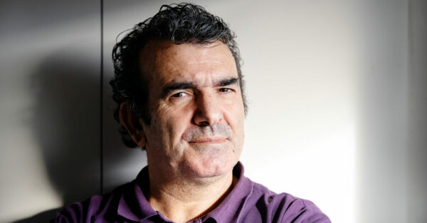 Porträttbild på Parvis Alizadeh. Han står framför en vit bakgrund och hans pikétröja är lila.