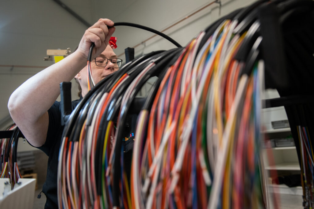 Carina arbetar med de stora kablarna som hänger på en ställning. Det är färgglada kablar. 
