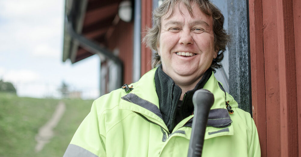 Bild på en glad kille som står utomhus mot en röd husvägg. Han bär reflexjacka och ler.