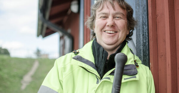 Bild på en glad kille som står utomhus mot en röd husvägg. Han bär reflexjacka och ler.