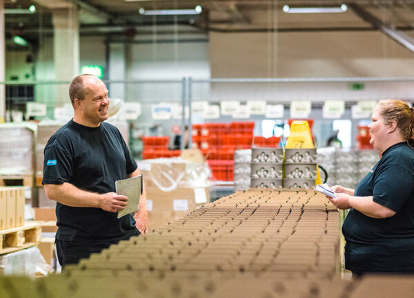 Två medarbetare på en postterminal, de har flera lådor mellan varandra, de tittar på varandra och ler.