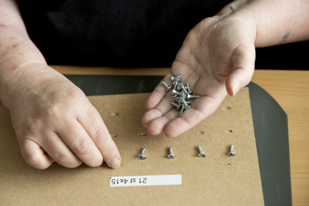 Bild på händer som arbetar med skruvar. Den ena handen håller i dem och den andra placerar dem på bordet. 