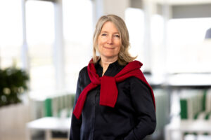 porträtt på en kvinna som har blont hår och svart skjorta. Hängades över axlarna är en röd tröja. 