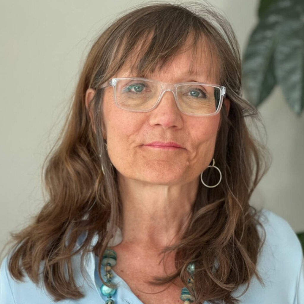 Porträtt på en kvinna med brunt hår och transparenta glasögon. Ljusblå tröja. 