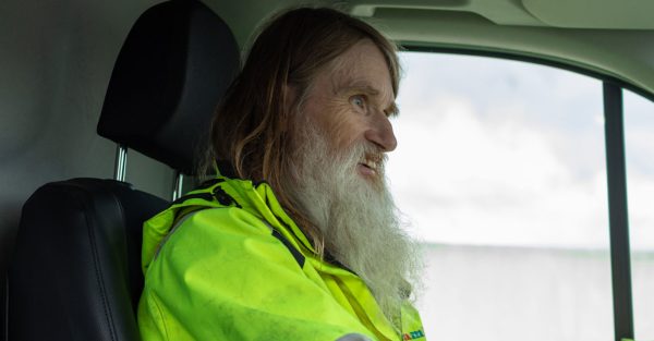 Bild på en man i signalfärgad jacka som kör bild. Mannen har grått långt hår.